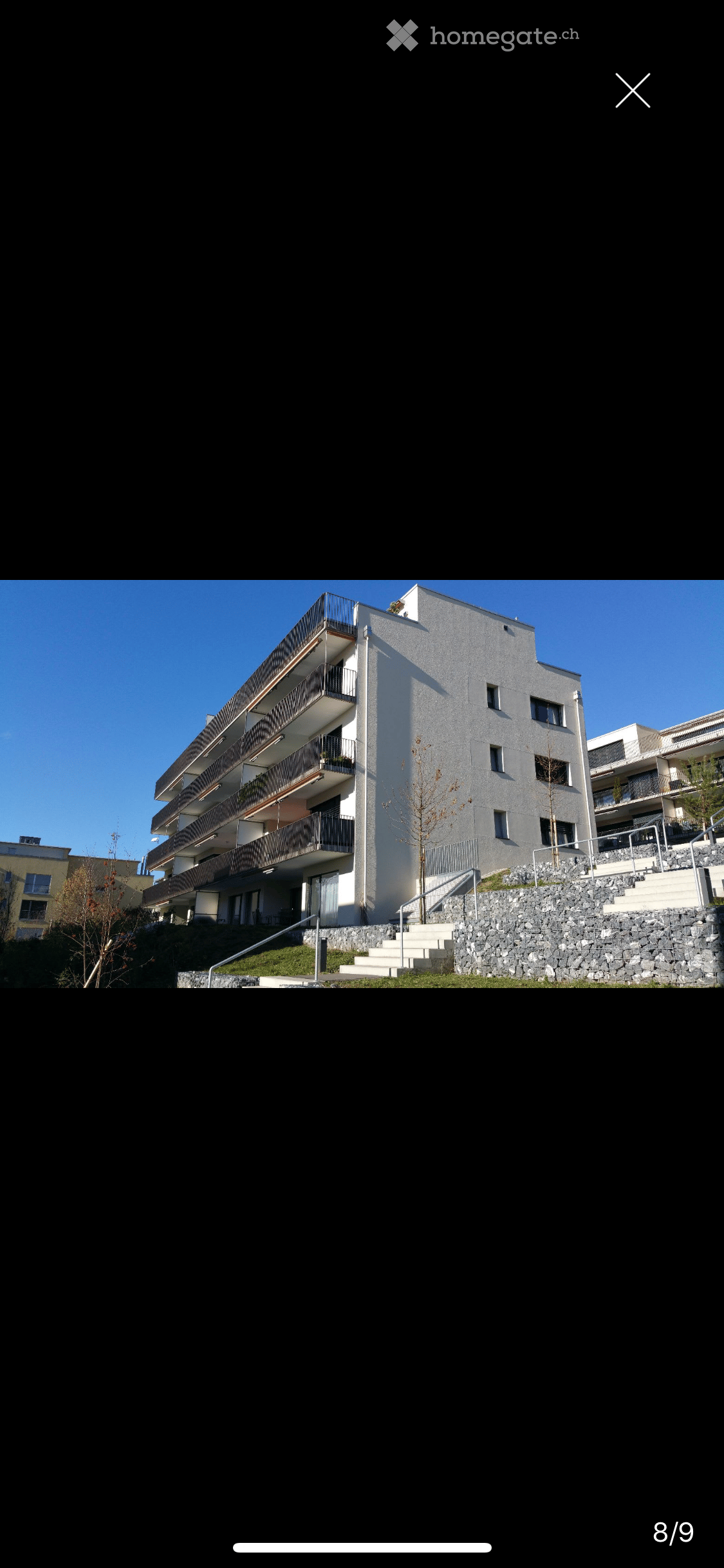 Modern multi-story residential building with balconies, raised ground floor, and stone staircase leading up to the entrance.
