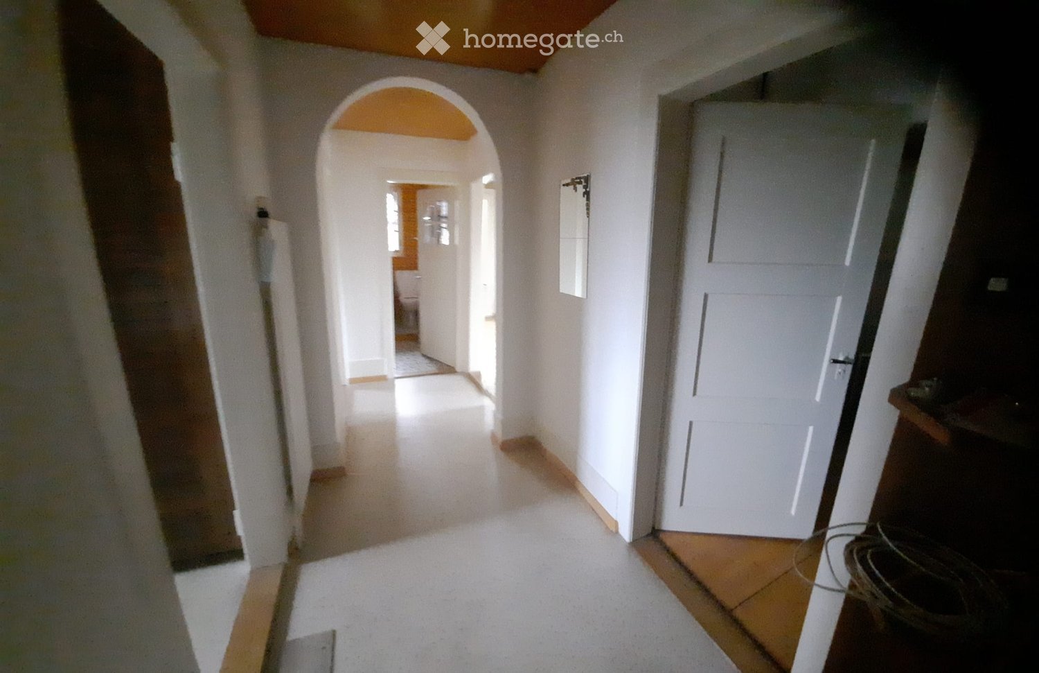 Empty hallway with white walls, carpeted floor, and an arched doorway leading to another room. A closed white door is visible on the right side.