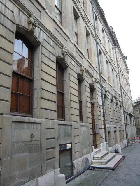 Gray stone facade, large arched windows, brown wooden windows, brown door, multiple floors, street-side view