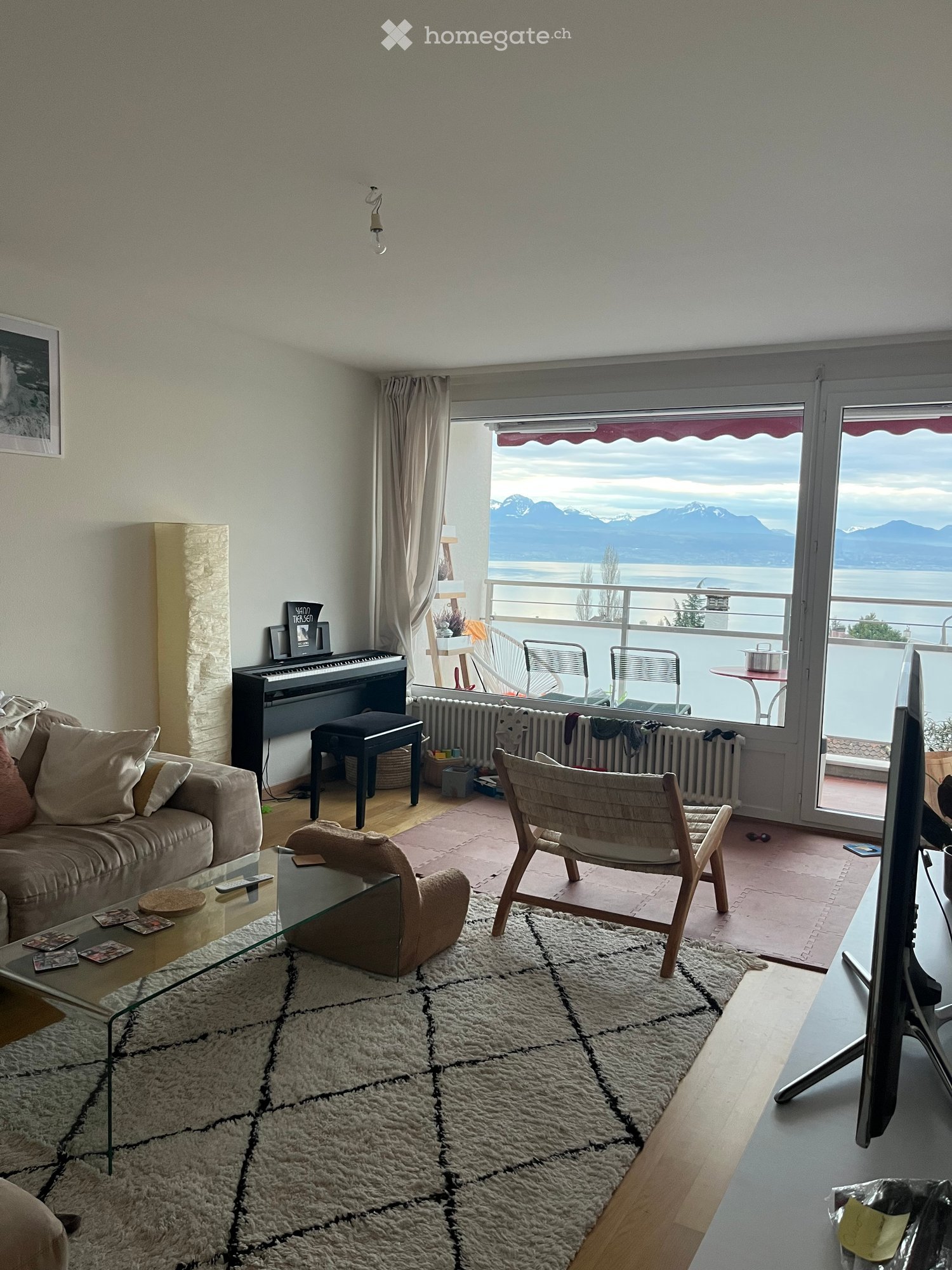 Living room with a view of mountains and water, featuring a sofa, coffee table, chair, piano, and television.