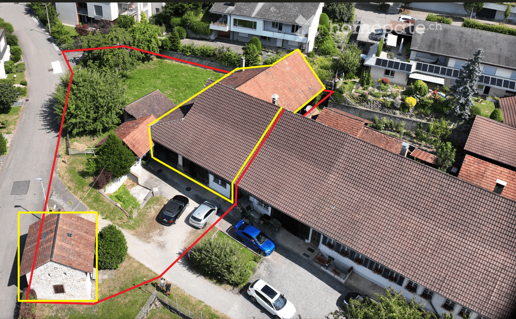 Aerial view of a residential building with a garage, multiple parked cars, and surrounding greenery.
