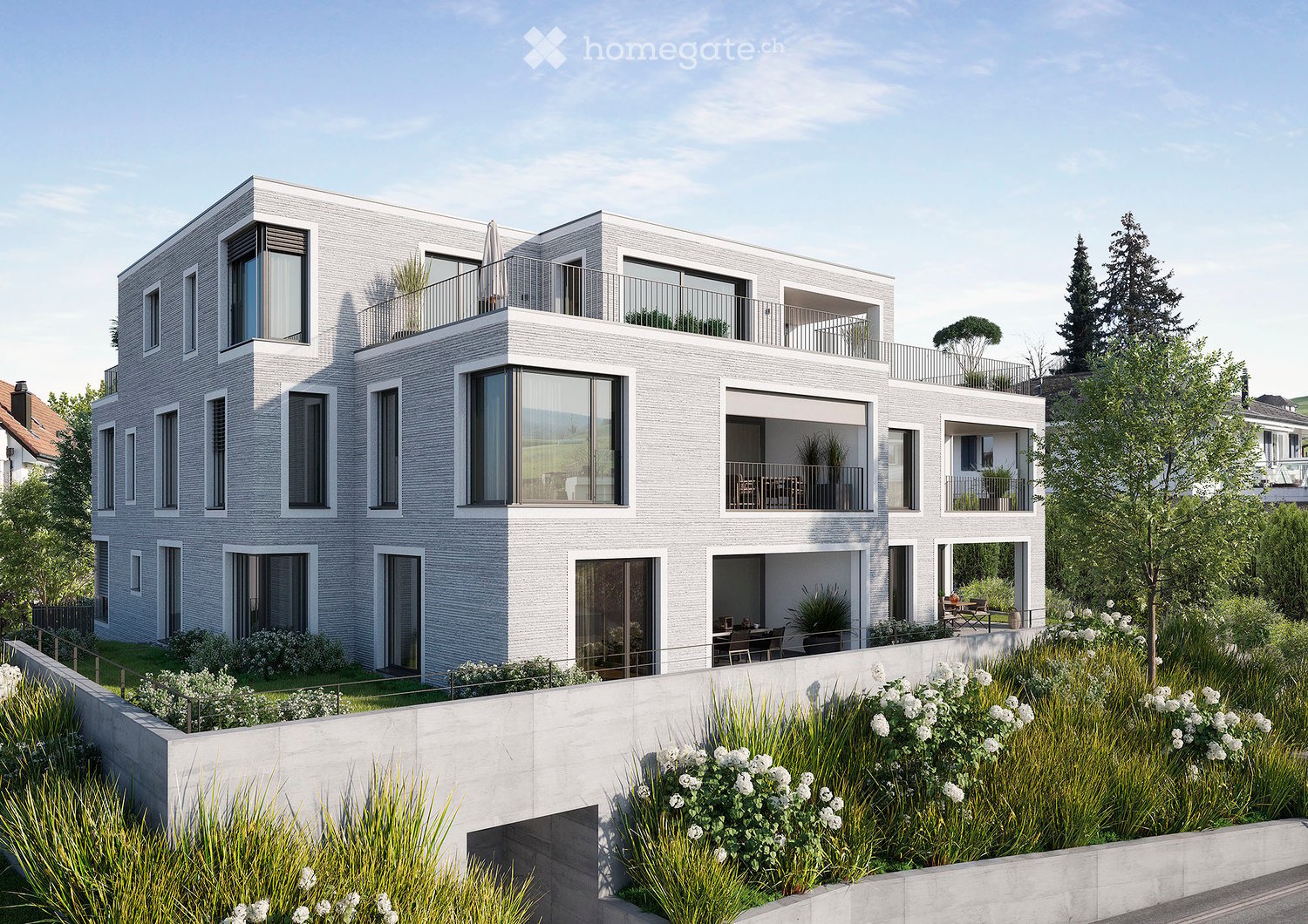 Modern two-story residential building with grey brick facade, large windows, balconies, and surrounding greenery.