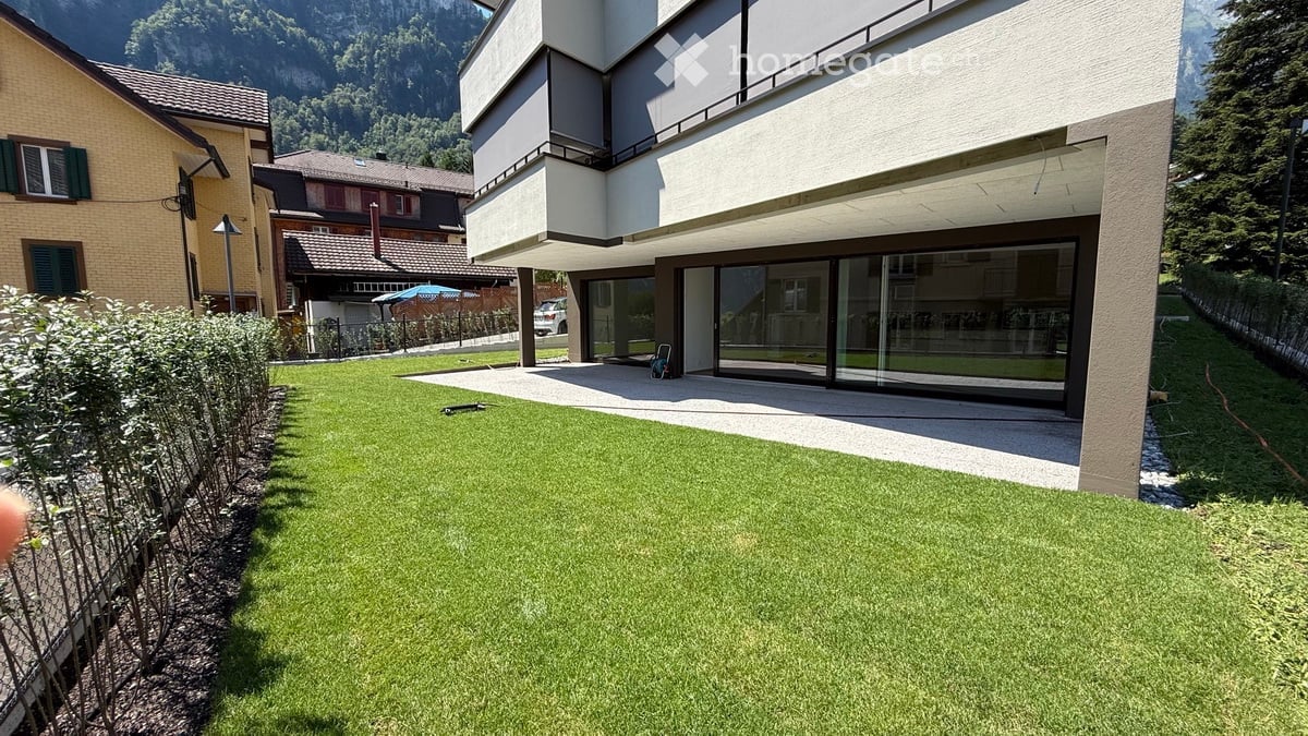 Well-maintained lawn with trimmed hedges, modern house with large glass windows, and surrounding greenery.