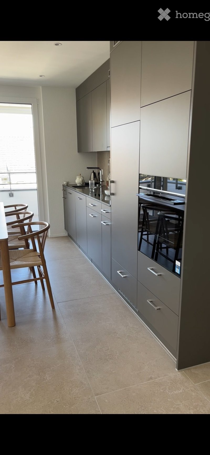 Modern kitchen with grey cabinets, a sink, faucet, oven, and a small dining area with chairs and a table.