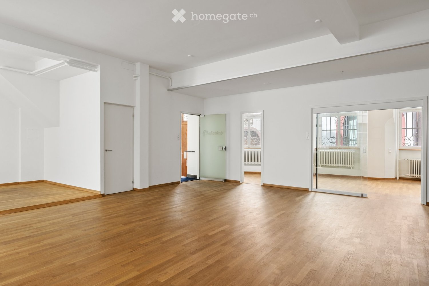 Empty room with wooden flooring, white walls, and multiple doors including a glass door leading to another space.