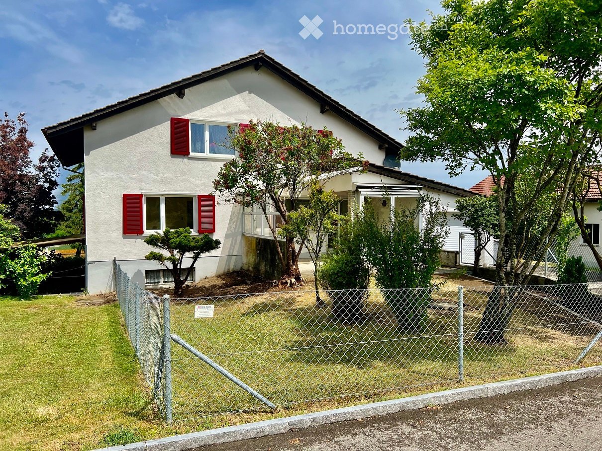 2 story house, white exterior, red shutters, fenced yard, trees, plants