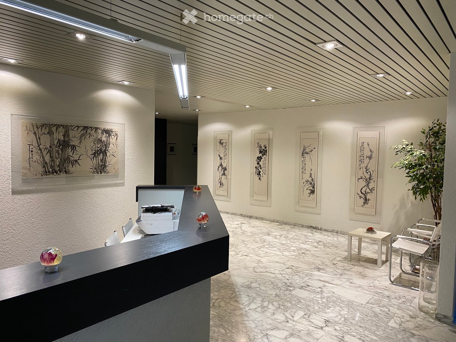 Modern reception area with a sleek black reception desk, white chairs, small table, printer, and framed artwork on the walls.