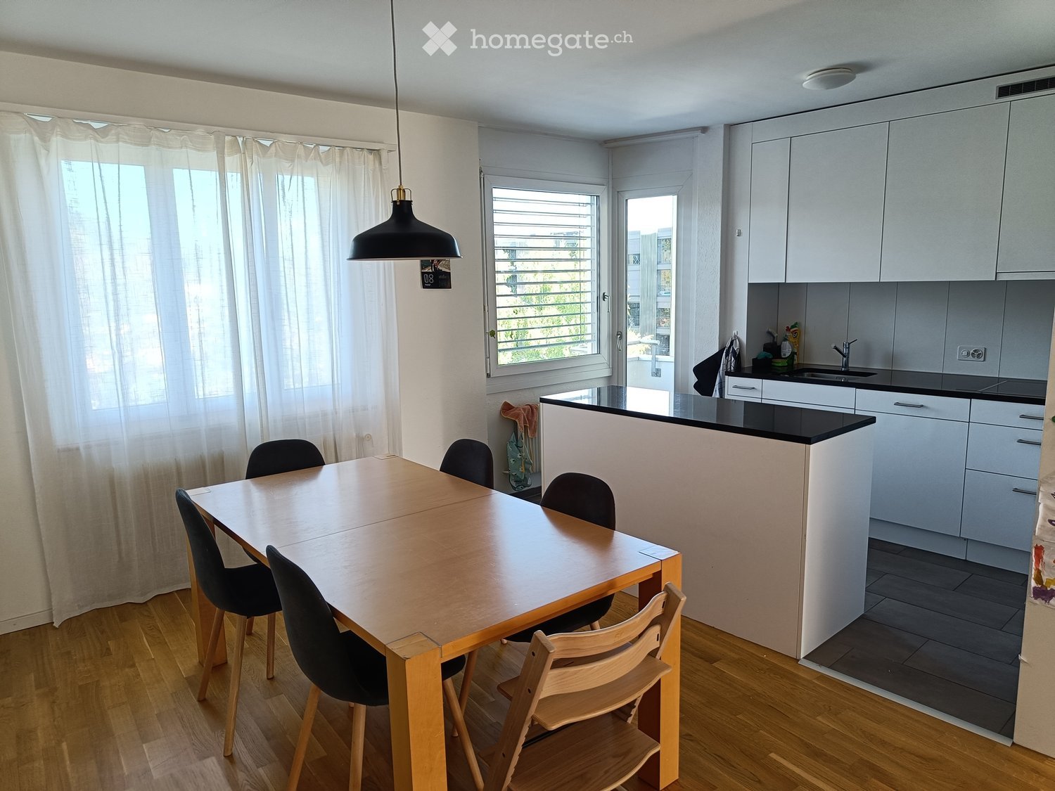 Modern dining area with a wooden table and chairs, adjacent to a white kitchen with cabinets and a sink.