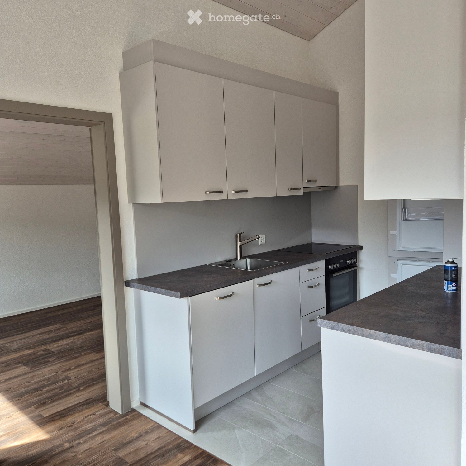 Modern kitchen with white cabinets, dark countertops, a sink, and an oven. The floor is wooden, and the walls are light-colored.