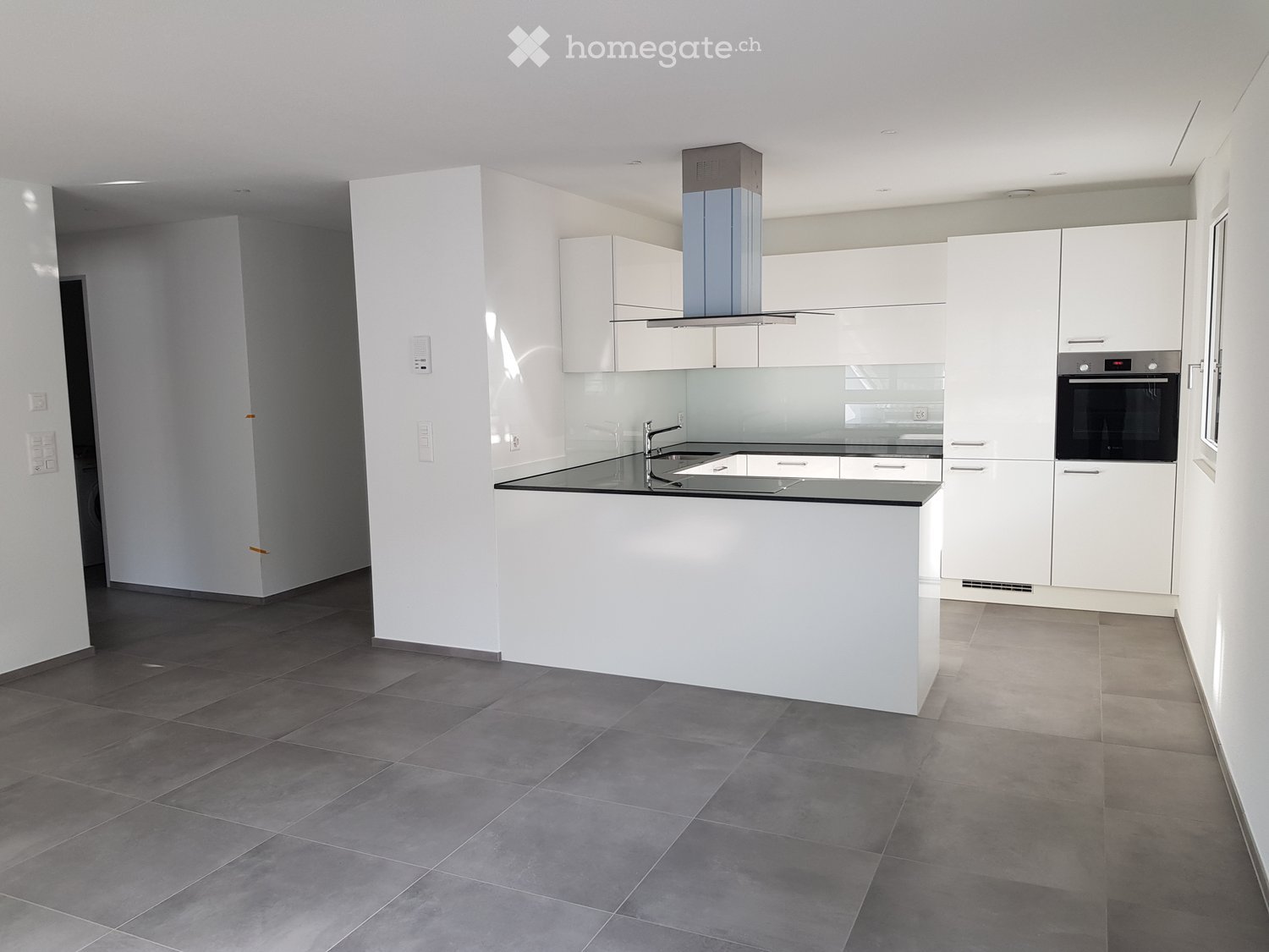 Modern kitchen with white cabinets, a central island, a sink, and an oven. The space features grey tiled flooring and a sleek, minimalist design.