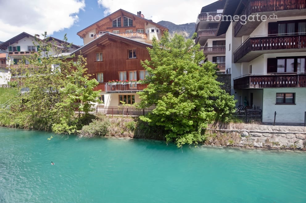 Scenic view of a Swiss village with traditional wooden houses, balconies, and a turquoise river flowing through the foreground.