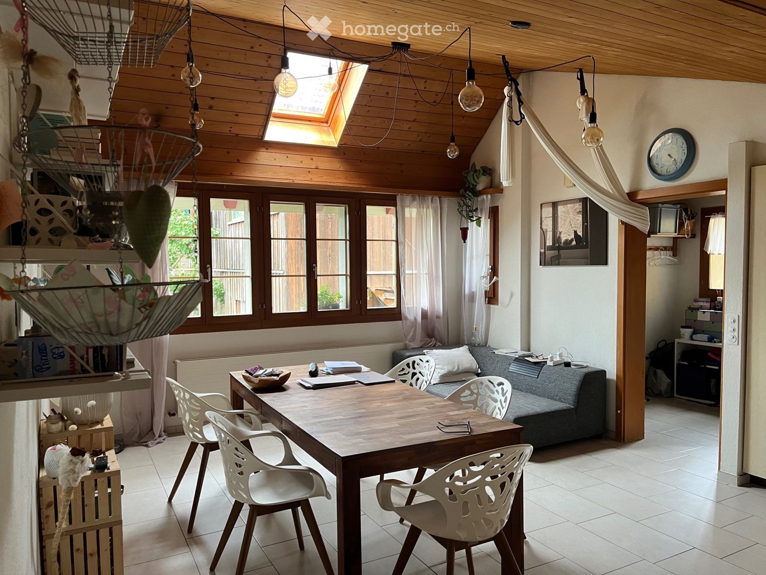 Bright living space with wooden ceiling, large windows, skylight, and skylight. Includes a dining table with chairs, a sofa, and decorative items.