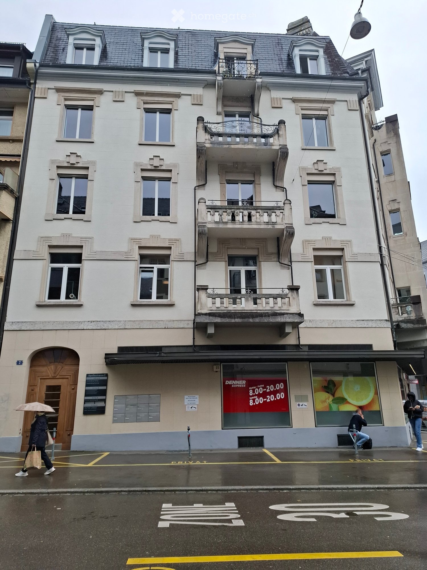 4 story white building with multiple balconies, storefronts, ground floor access door