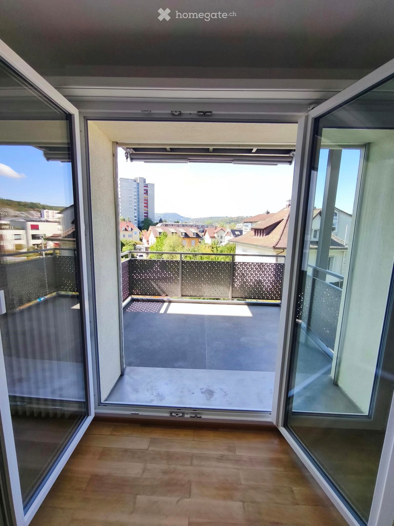 Balcony with glass doors, metal railing, and a view of the city and surrounding landscape.