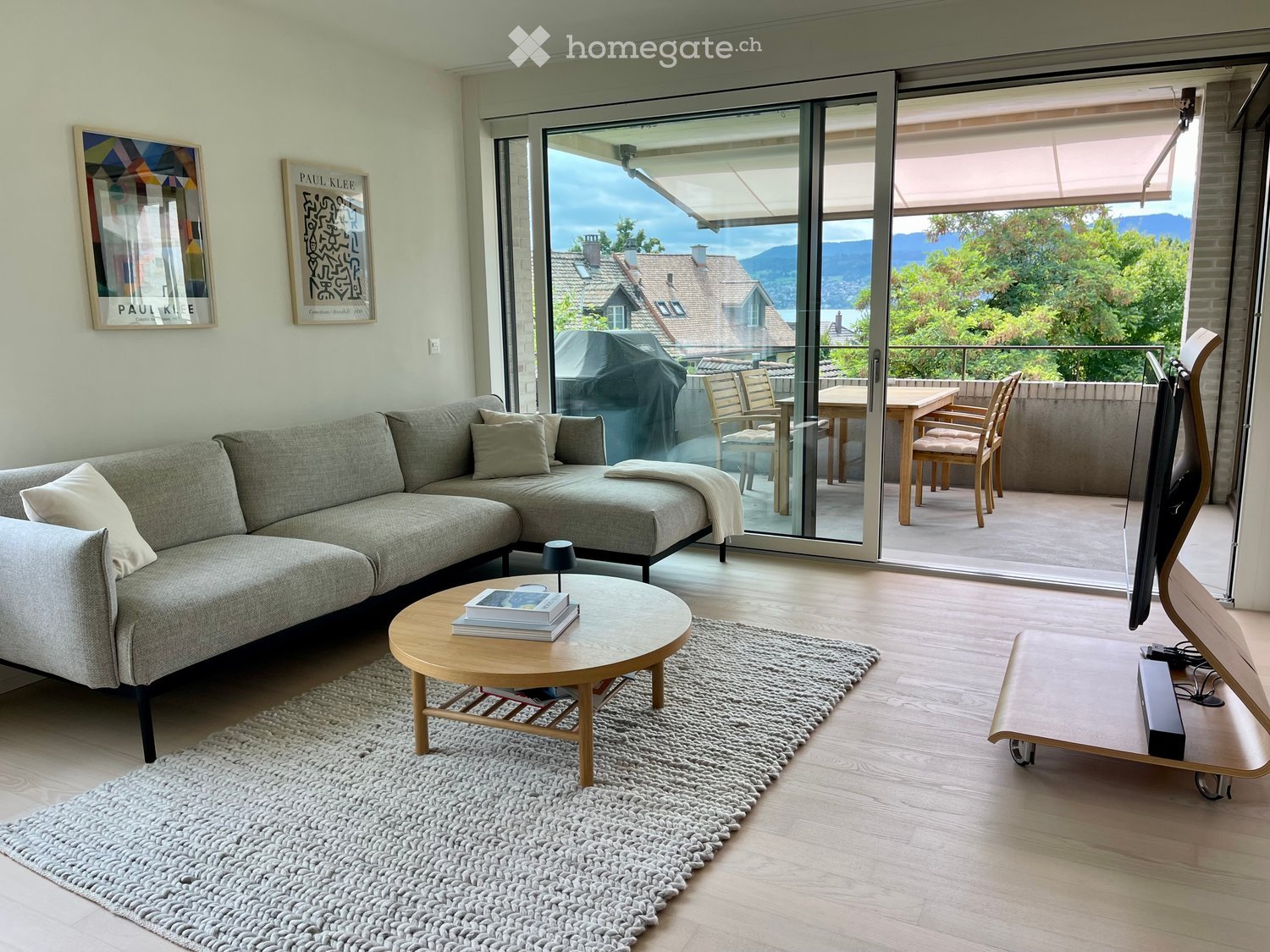 large L-shaped sofa, wooden coffee table, rug, glass sliding doors, balcony with outdoor dining set, TV