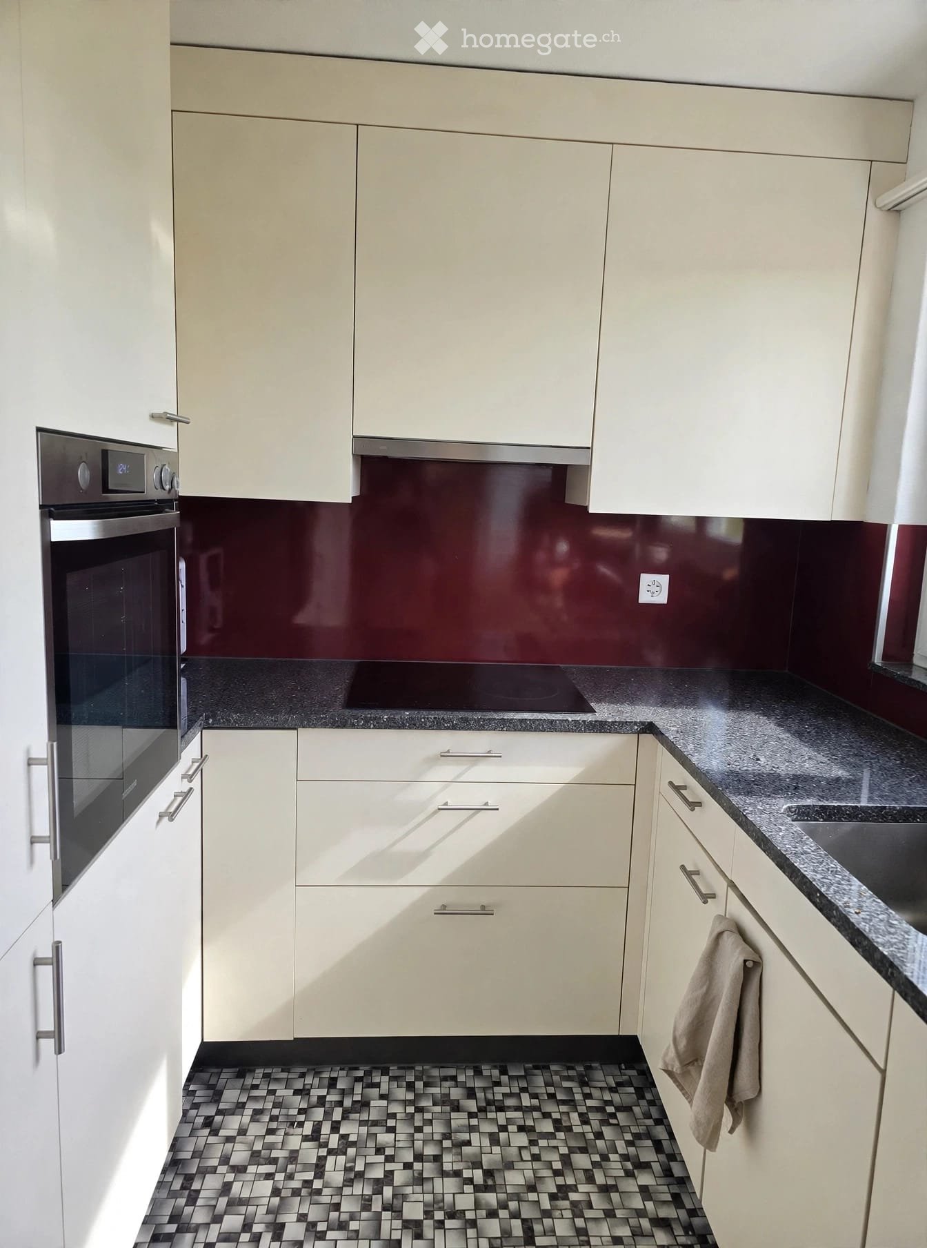 Modern kitchen with white cabinets, black granite countertops, and a dark backsplash. Features an oven, sink, and a towel hanging from a cabinet handle.