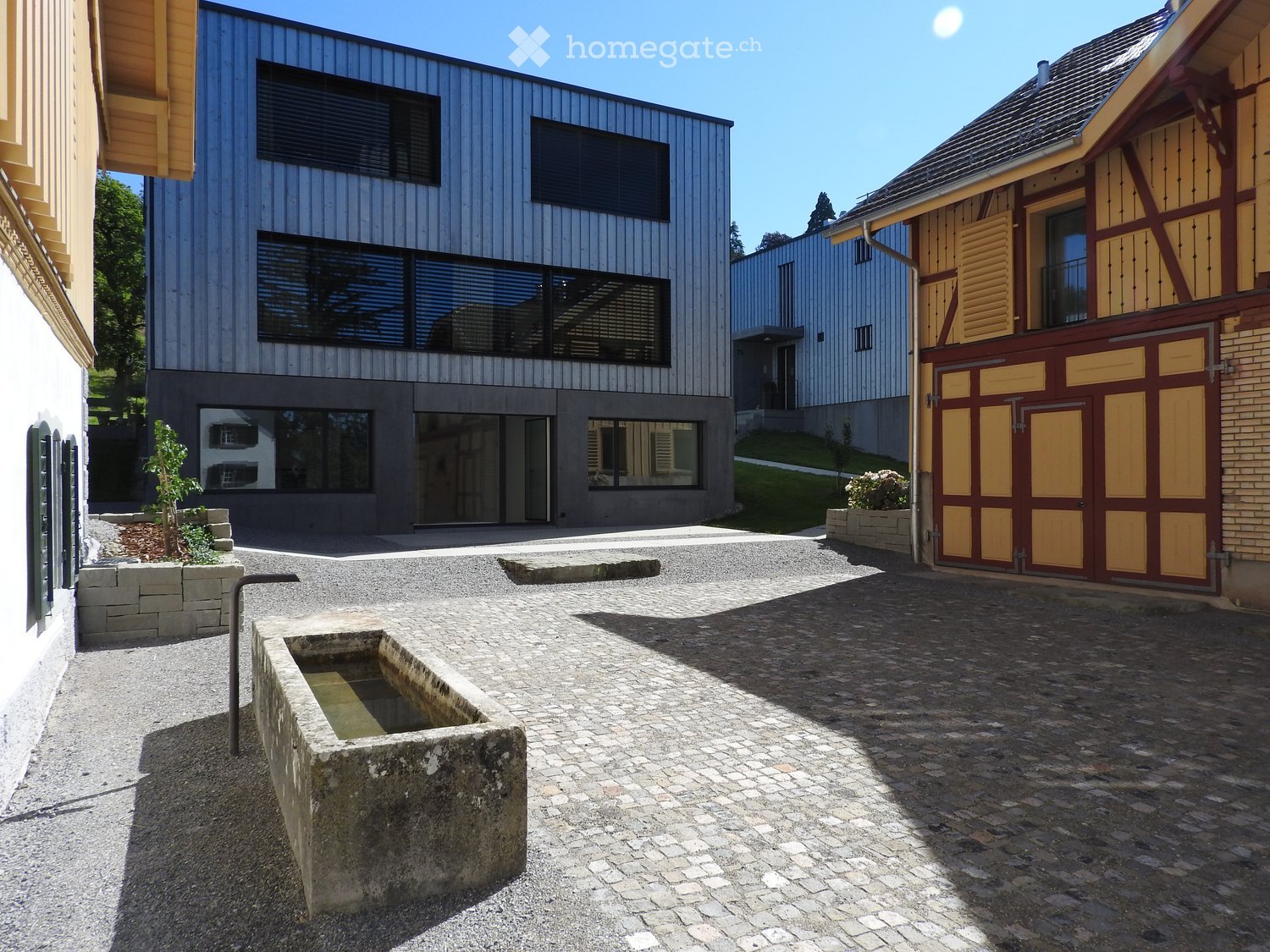 Modern house with gray exterior, large windows, and a paved courtyard.