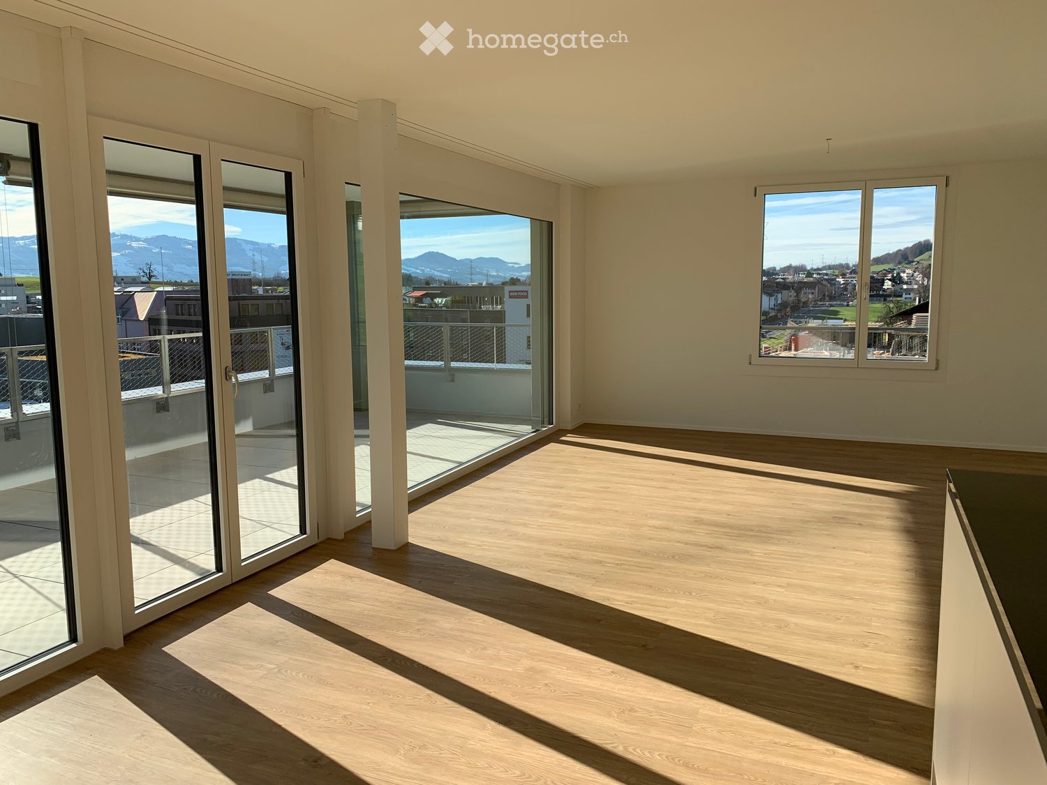 Empty room with wooden flooring, large glass sliding doors leading to a balcony, and windows offering a scenic mountain view.