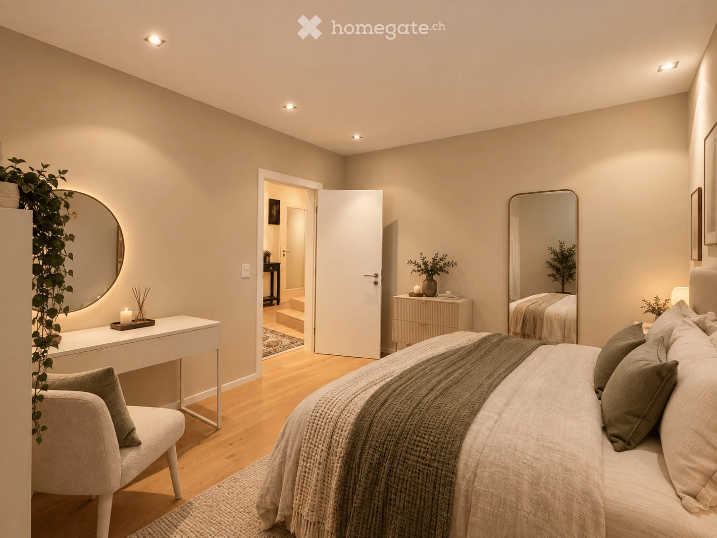 Modern bedroom with a large bed, a white vanity table, a round mirror, a small chair, and a drawer unit. The room features light wooden flooring and neutral-colored walls.