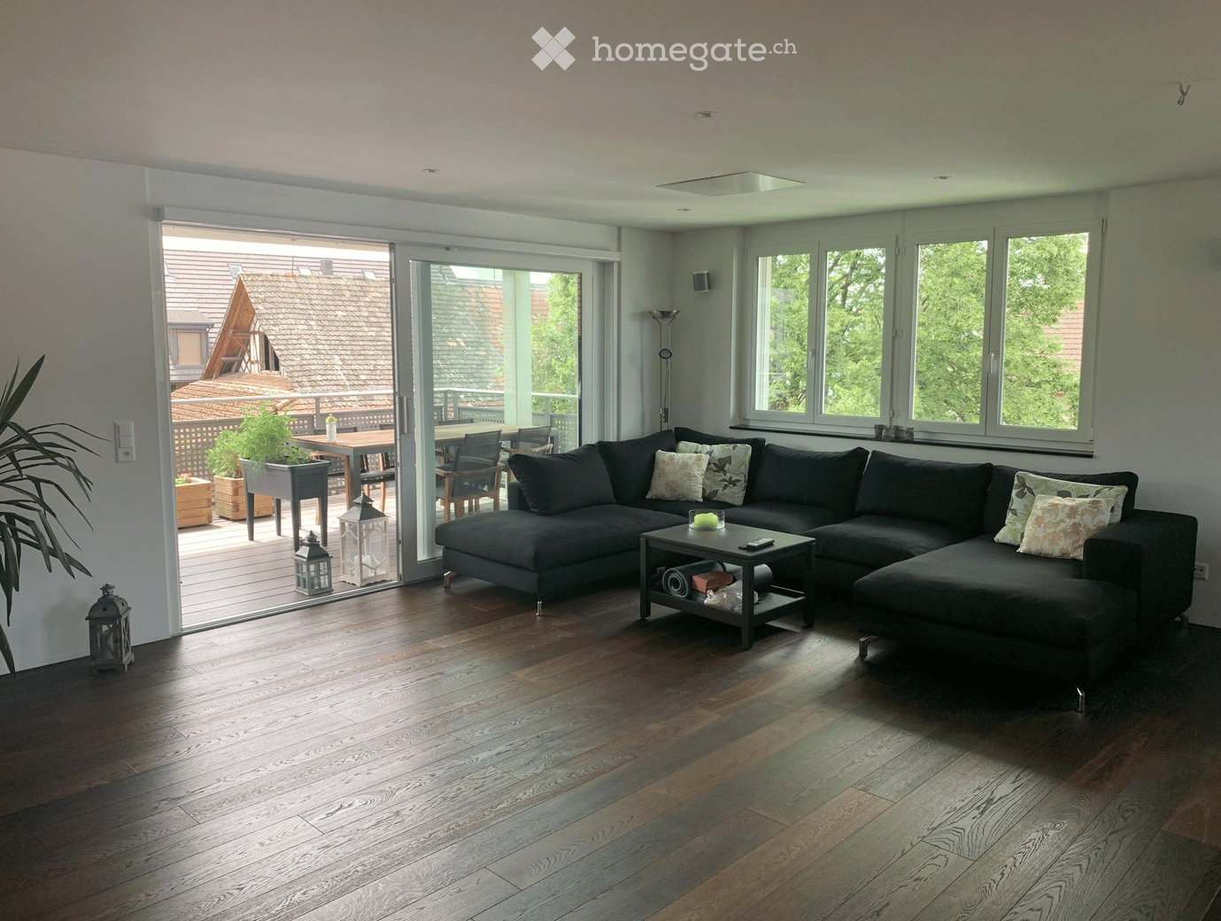 Modern living room with dark grey sectional sofa, coffee table, large windows, and sliding glass doors leading to a patio with outdoor furniture.