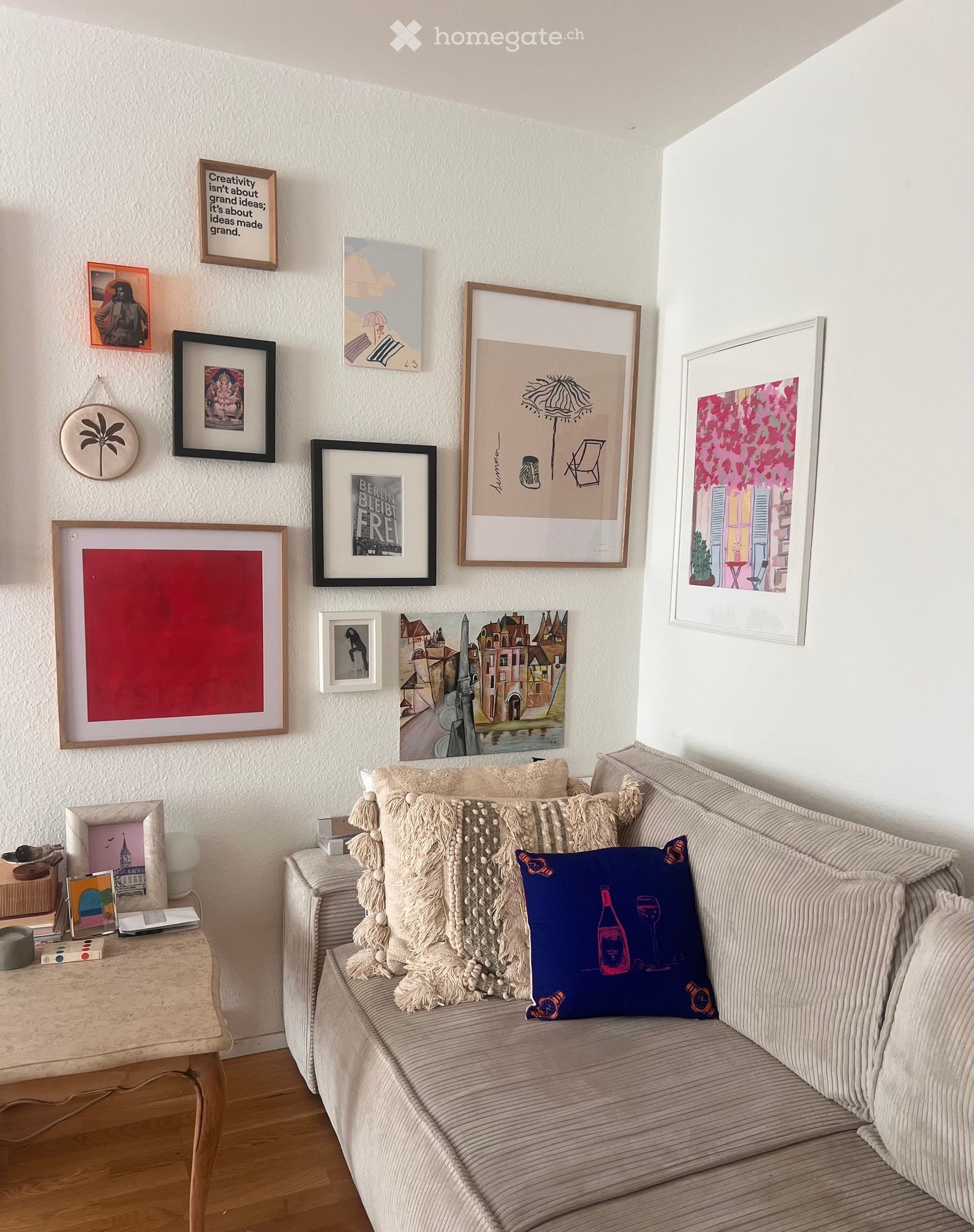 A cozy living room with a beige sofa adorned with pillows, a wooden coffee table, and a variety of framed artworks on the wall.