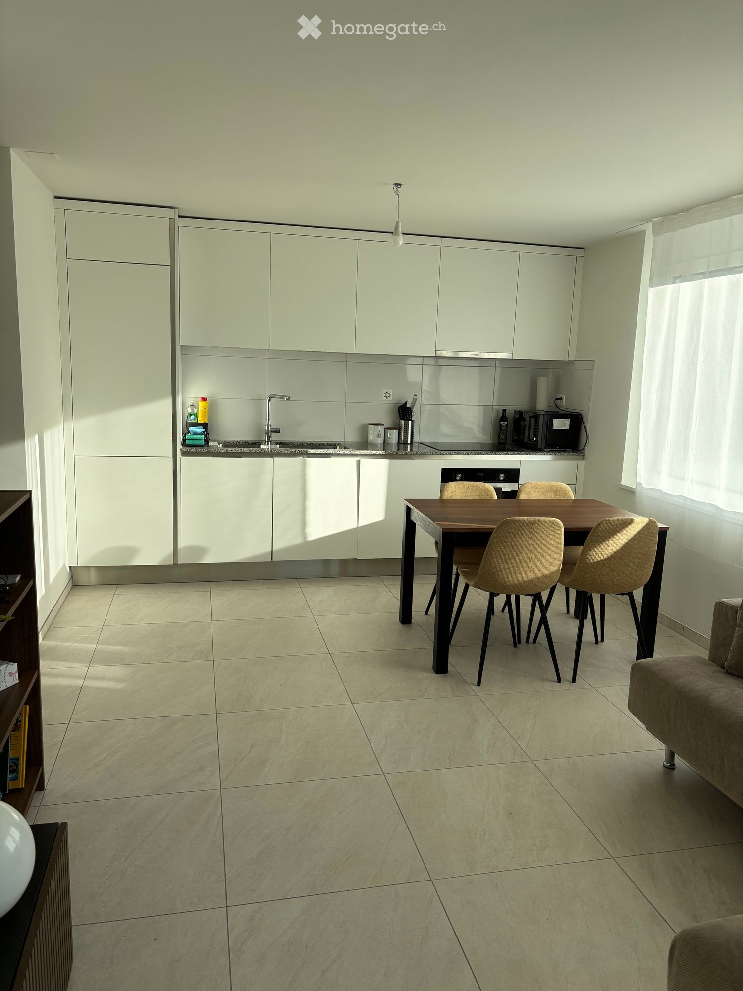 Modern kitchen and dining area with white cabinets, a central island, a dining table with four chairs, and a sofa in the corner.