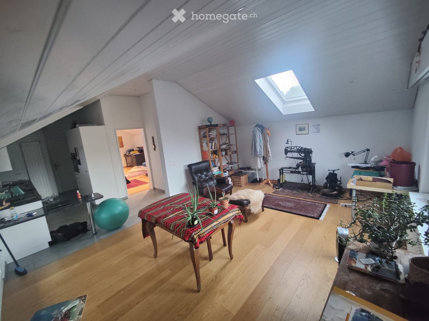 Bright, open attic space with wooden floors, skylight, and various furniture including a table, chairs, a ball, and a bookshelf.