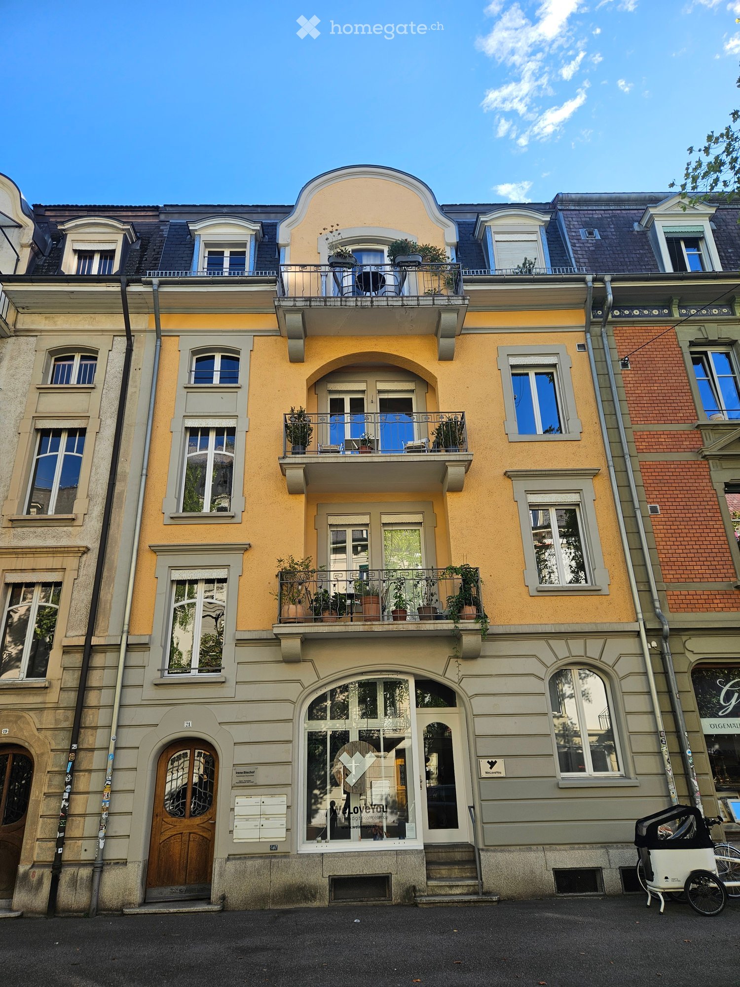 Multi-story residential building with yellow facade, multiple balconies, and decorative architectural details.