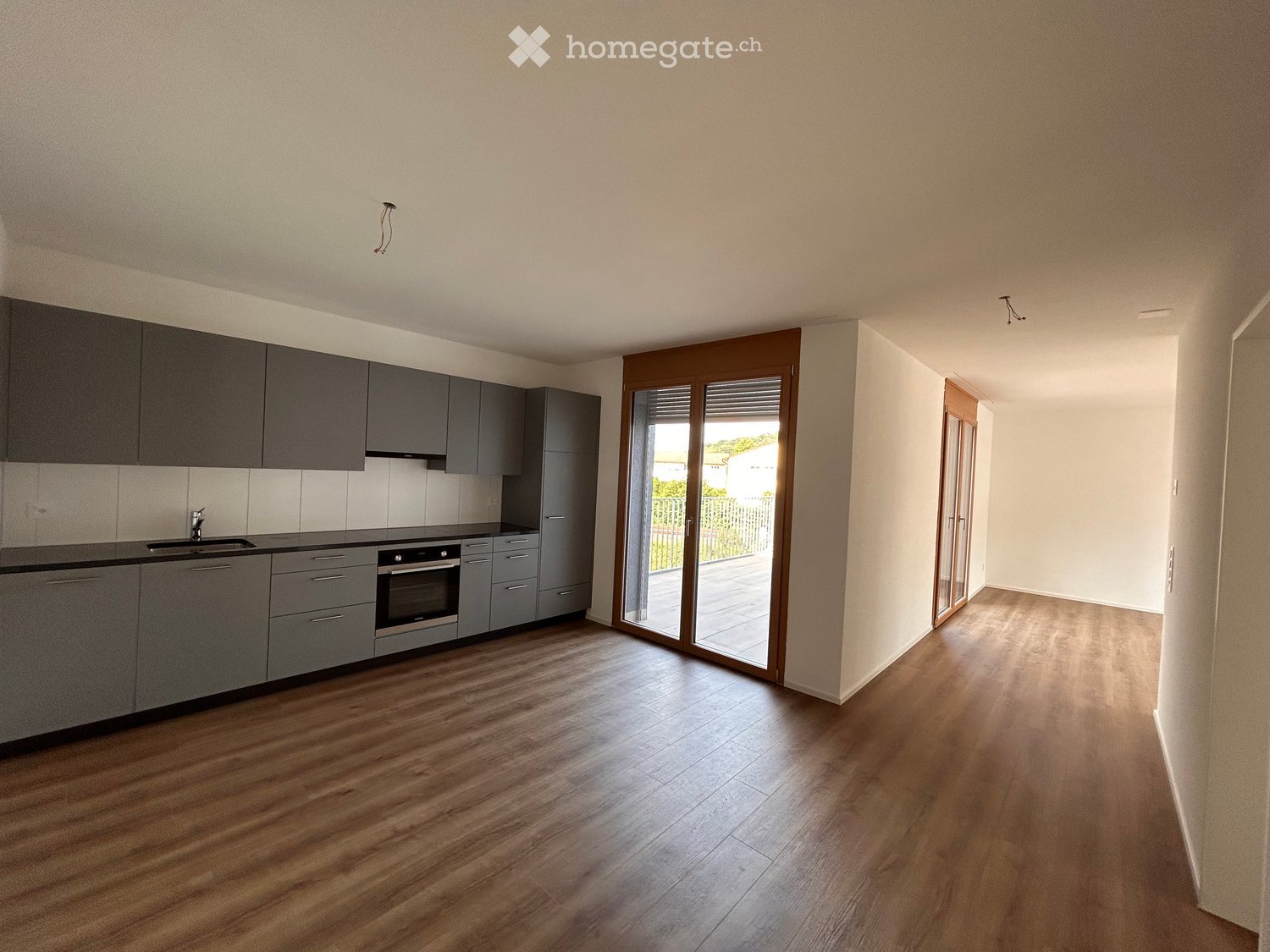Kitchen with wooden floors, gray cabinets, black countertops, built-in oven, sink, sliding doors to a terrace