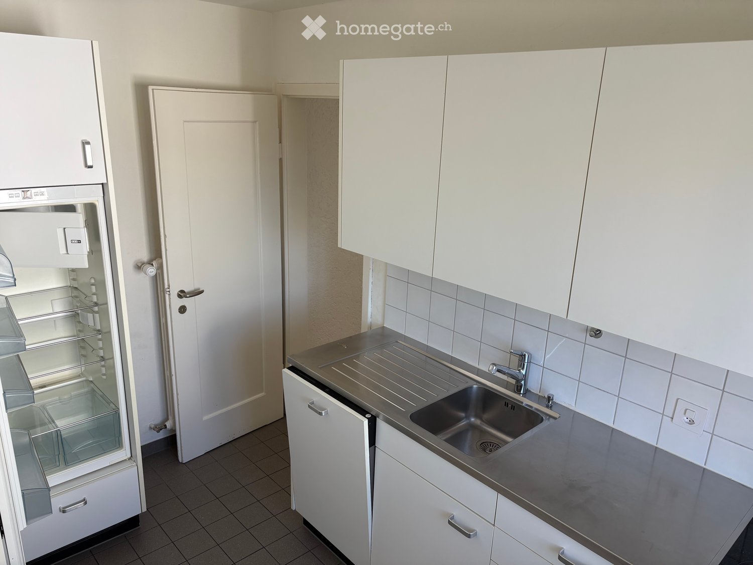 Modern kitchen with white cabinets, stainless steel sink, and a refrigerator with glass doors.