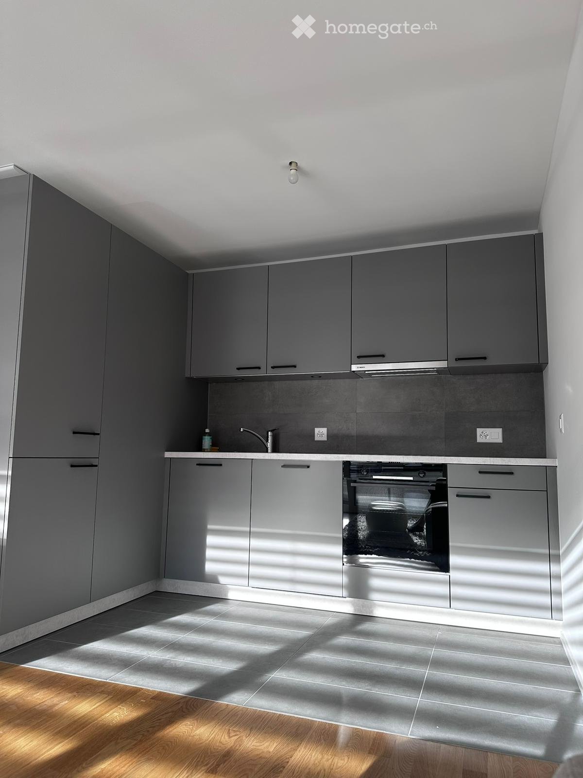 Modern kitchen with grey cabinets, stainless steel oven, and wooden flooring.