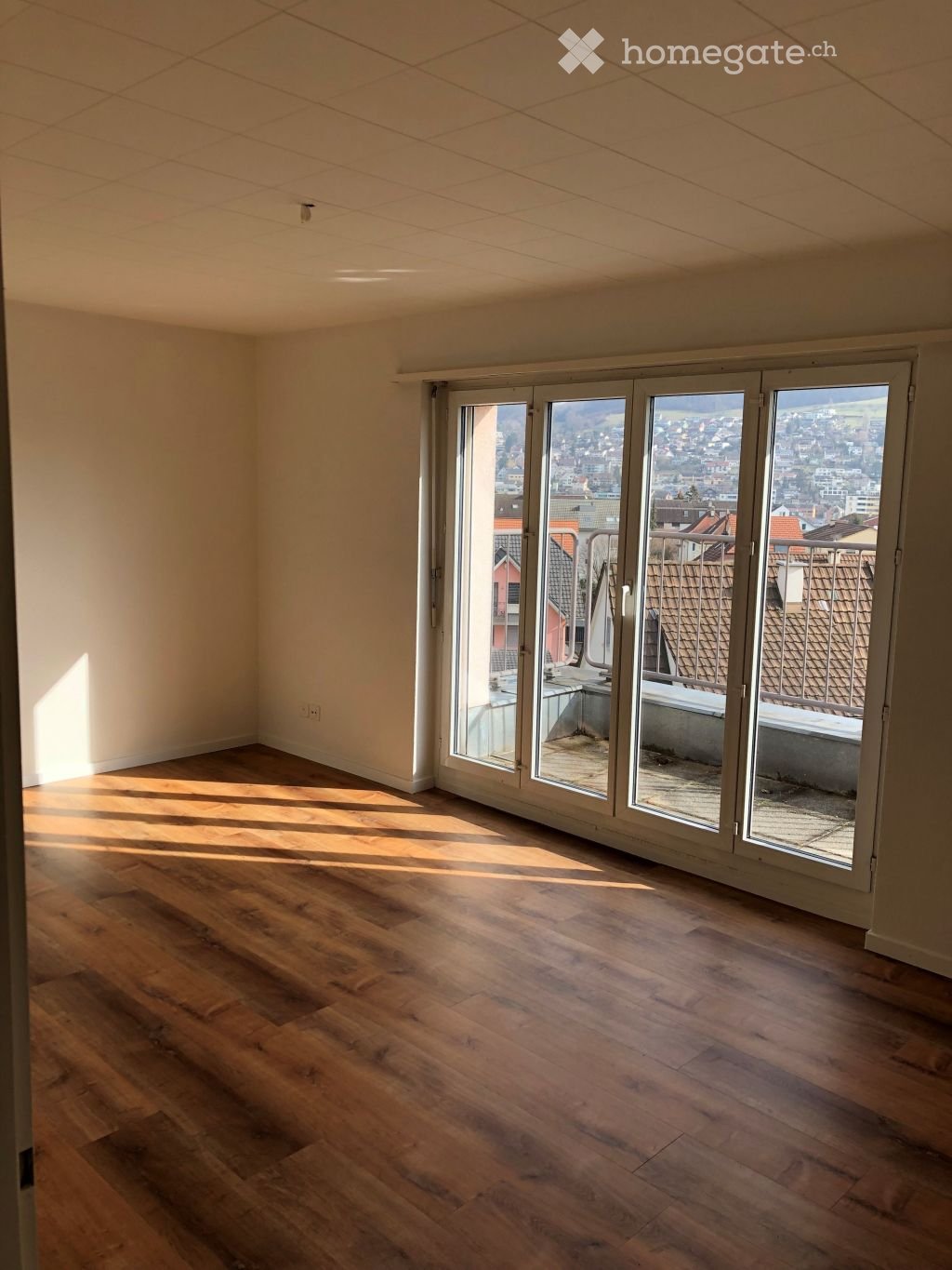 Empty room with wooden flooring and large glass sliding doors leading to a balcony with a city view.
