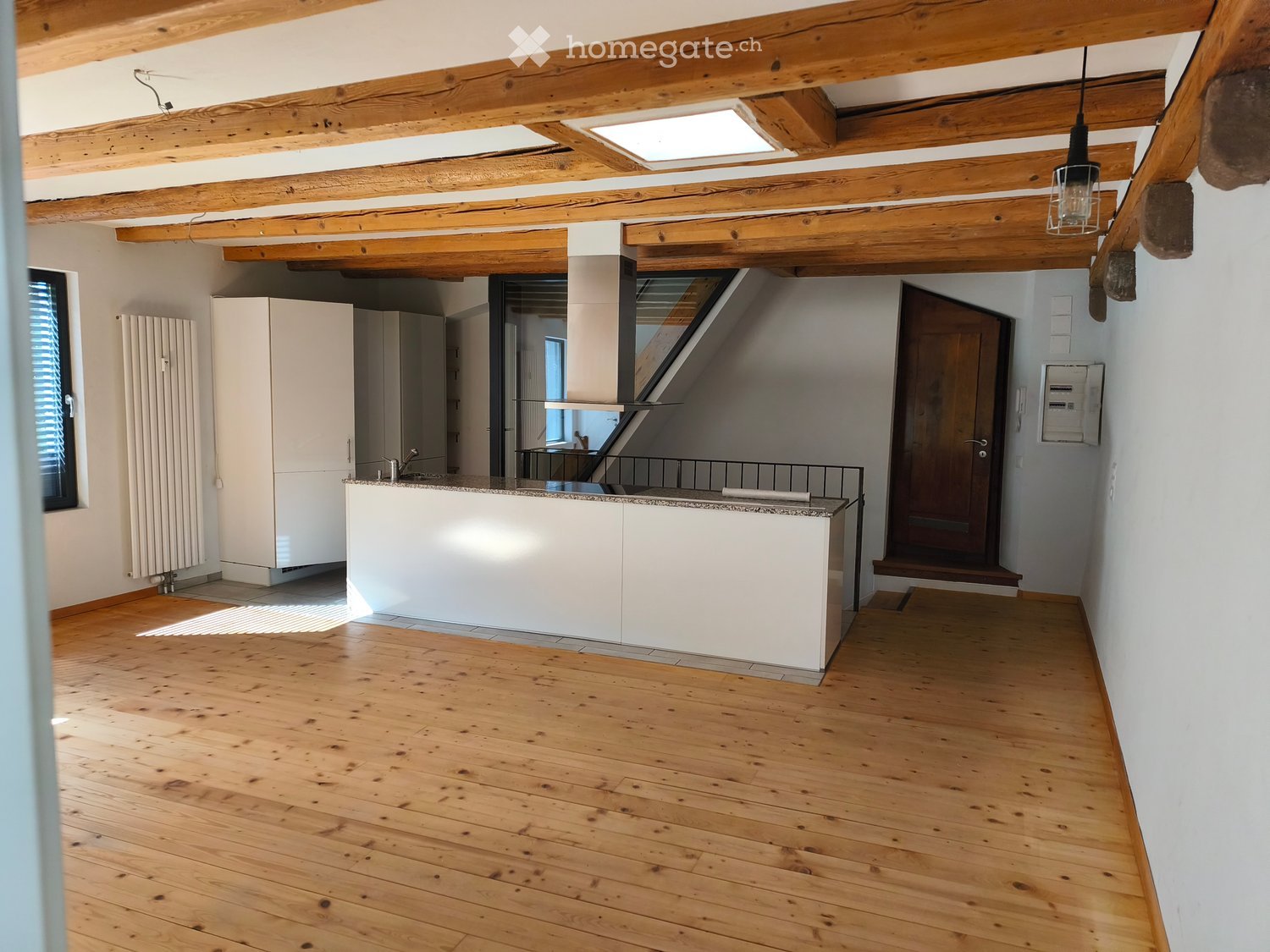 Open-plan kitchen area with wooden floors, white cabinets, a kitchen island, and a staircase leading to an upper level.