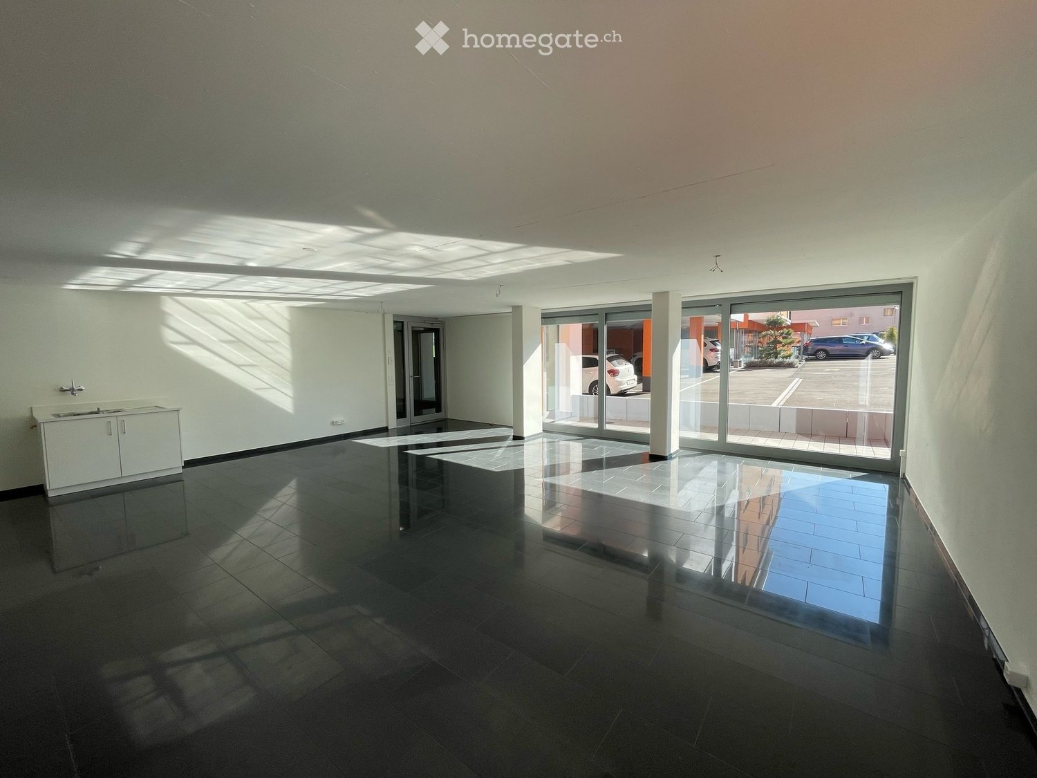 empty room, large windows, sliding doors, tiled floor, kitchen area with sink, white walls, overhead lighting
