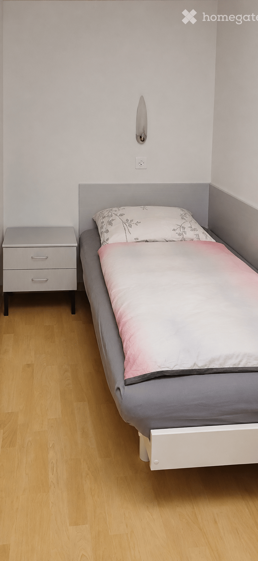 Modern bedroom with a single bed, grey bedding, pink accent pillow, and a matching nightstand.