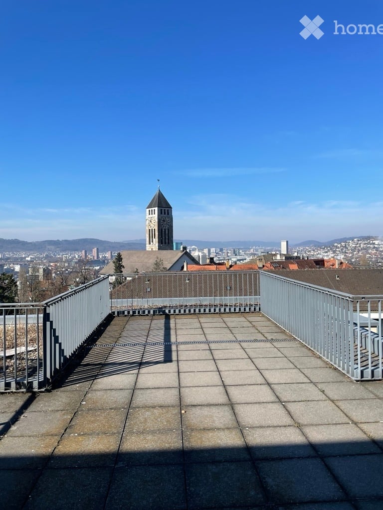 Roof terrace with metal railings, tiled floor, and a panoramic cityscape view including a clock tower and distant buildings.
