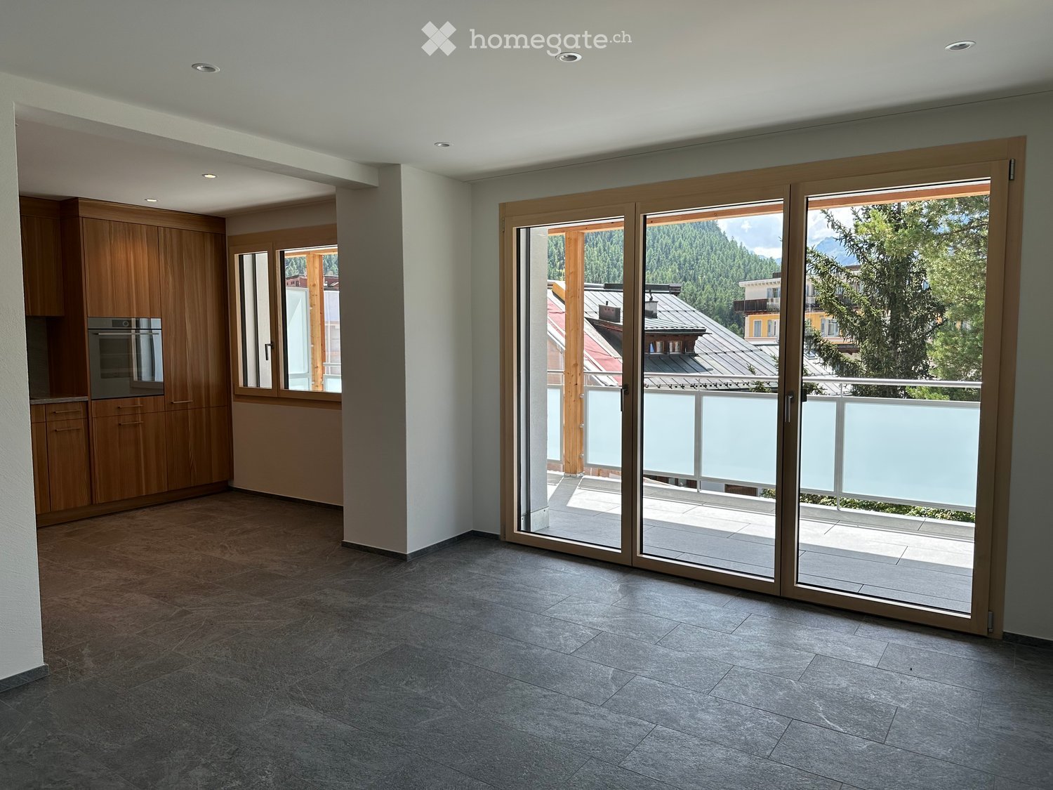 Empty room with large sliding glass doors leading to a balcony, wooden cabinets, and a view of the surrounding landscape.