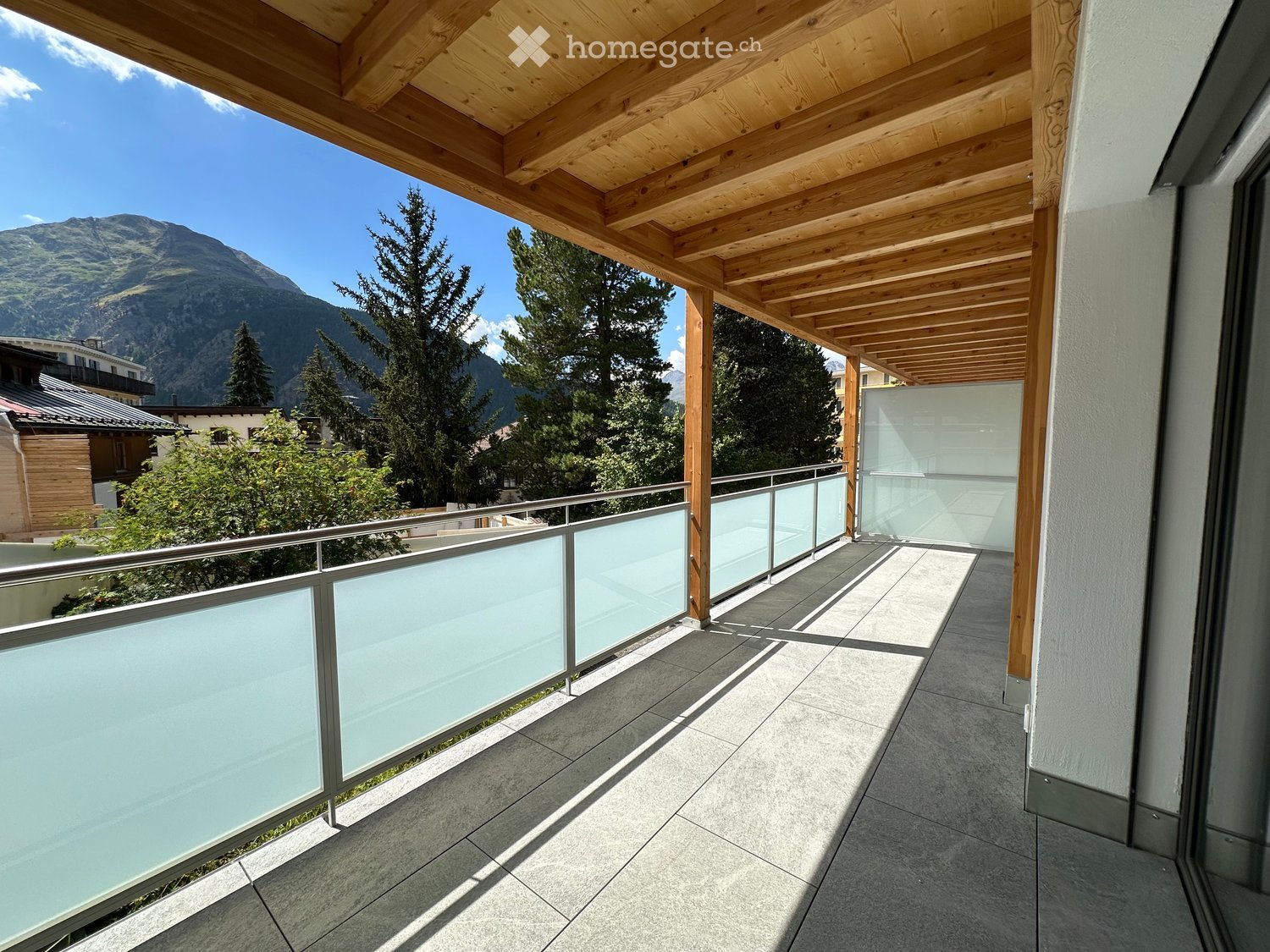 Balcony with wooden pergola, glass railing, and a view of mountains and trees.