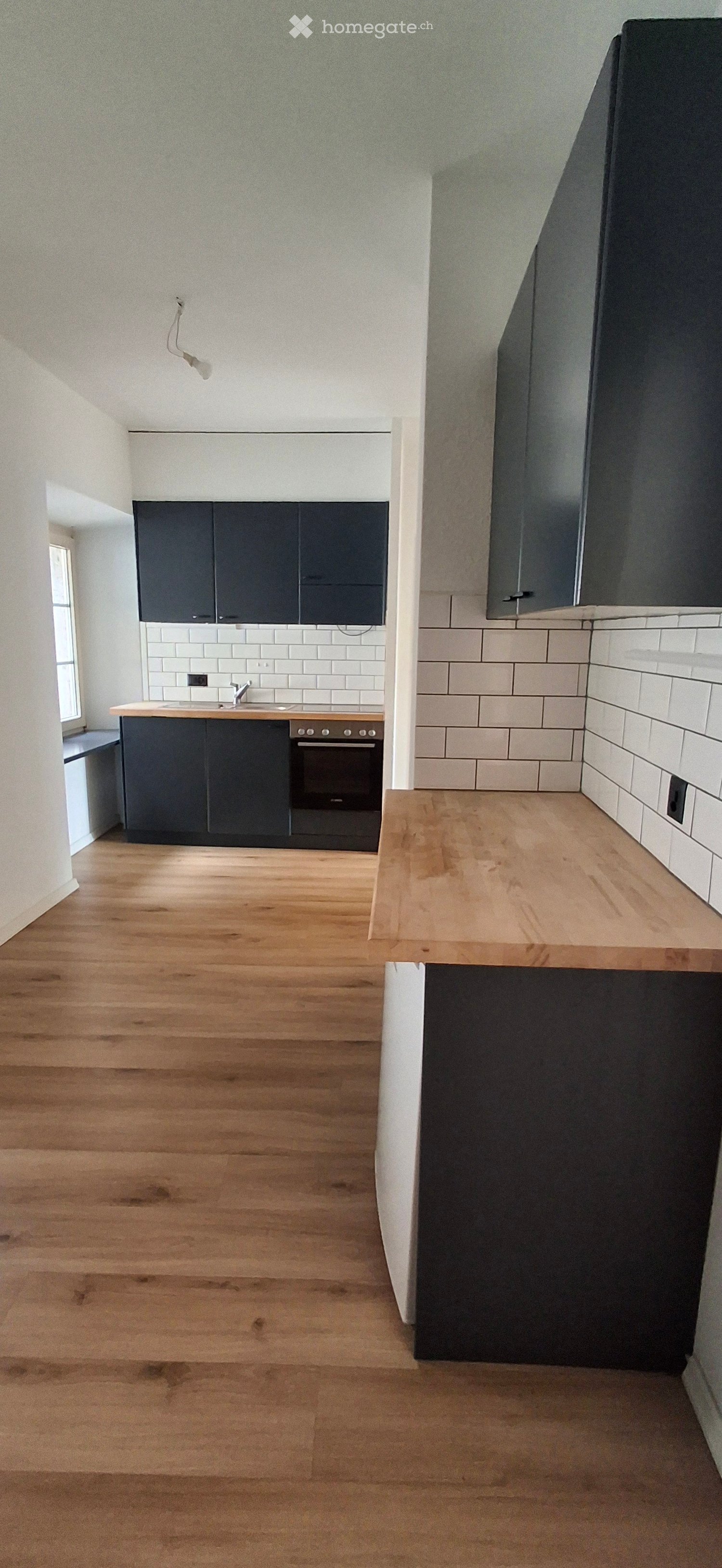 Empty kitchen with dark cabinets, white tiled backsplash, wooden floor, and a wooden island. No appliances or furniture are present.