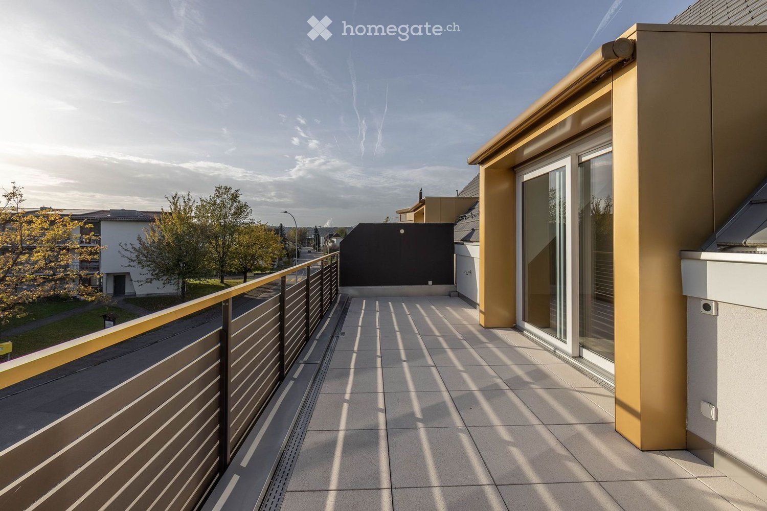Modern balcony with tiled floor, metal railing, and glass door leading to a building.