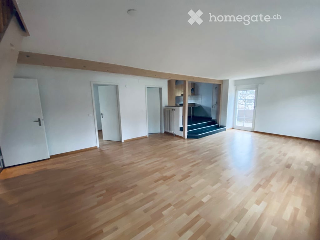 Empty room with wooden flooring, white walls, and several doors leading to other spaces. No furniture or equipment is present.