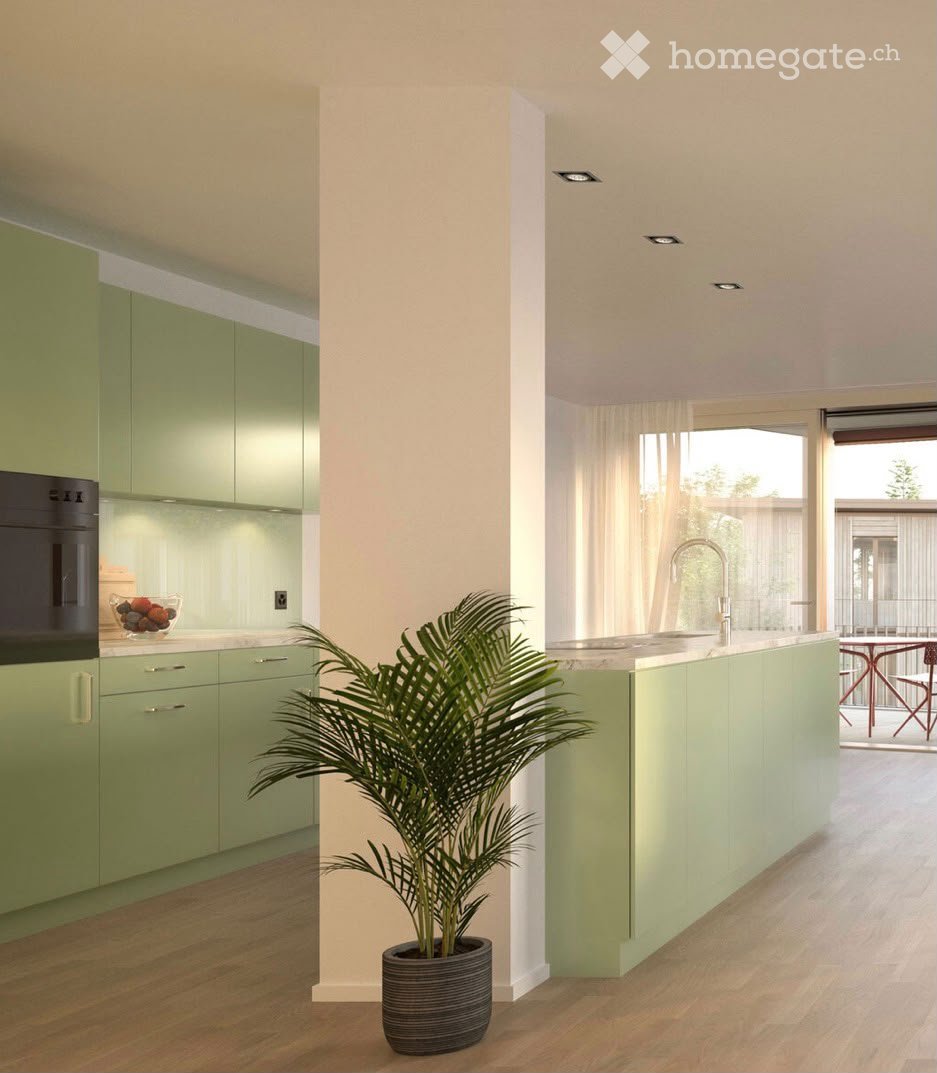 Modern kitchen with green cabinets, a central island, a potted plant, and a bowl of fruit on the counter.