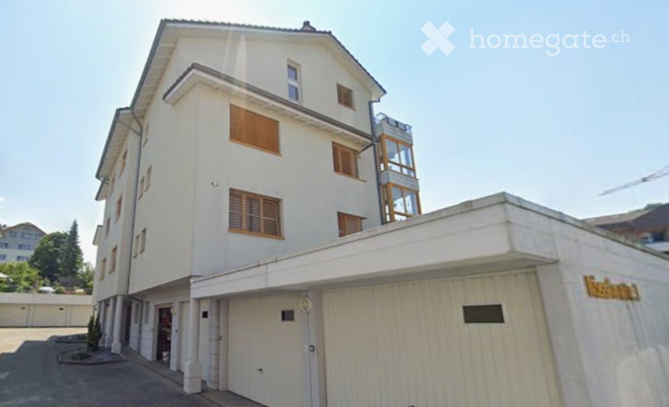 Modern multi-story building with white facade, wooden shutters, and a garage entrance.