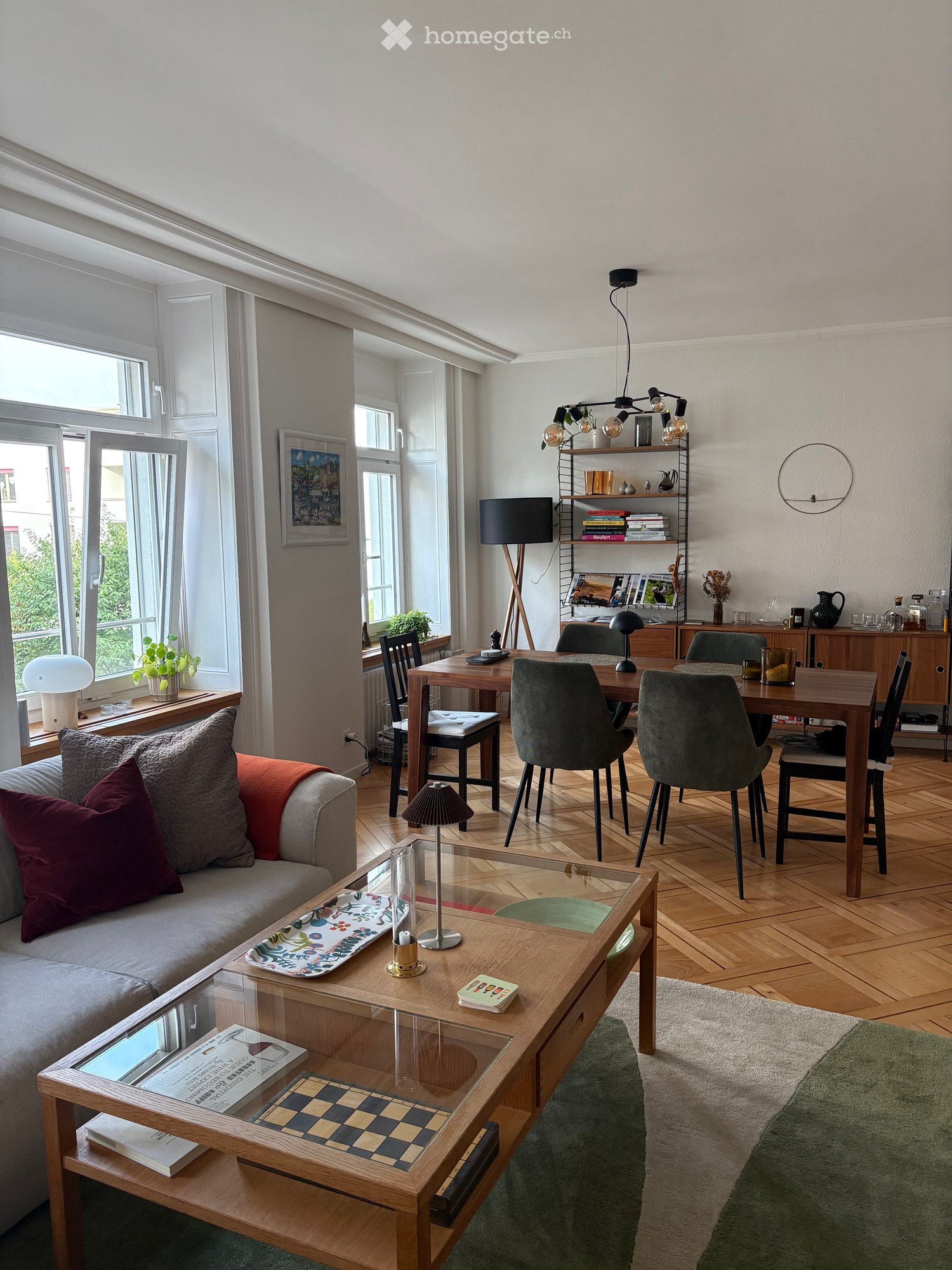A modern, well-lit living and dining area with a grey sofa, wooden coffee table, dining table with chairs, floor lamp, and decorative items.