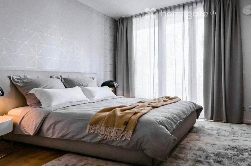 Modern bedroom with a large bed, nightstand, lamp, and grey curtains.