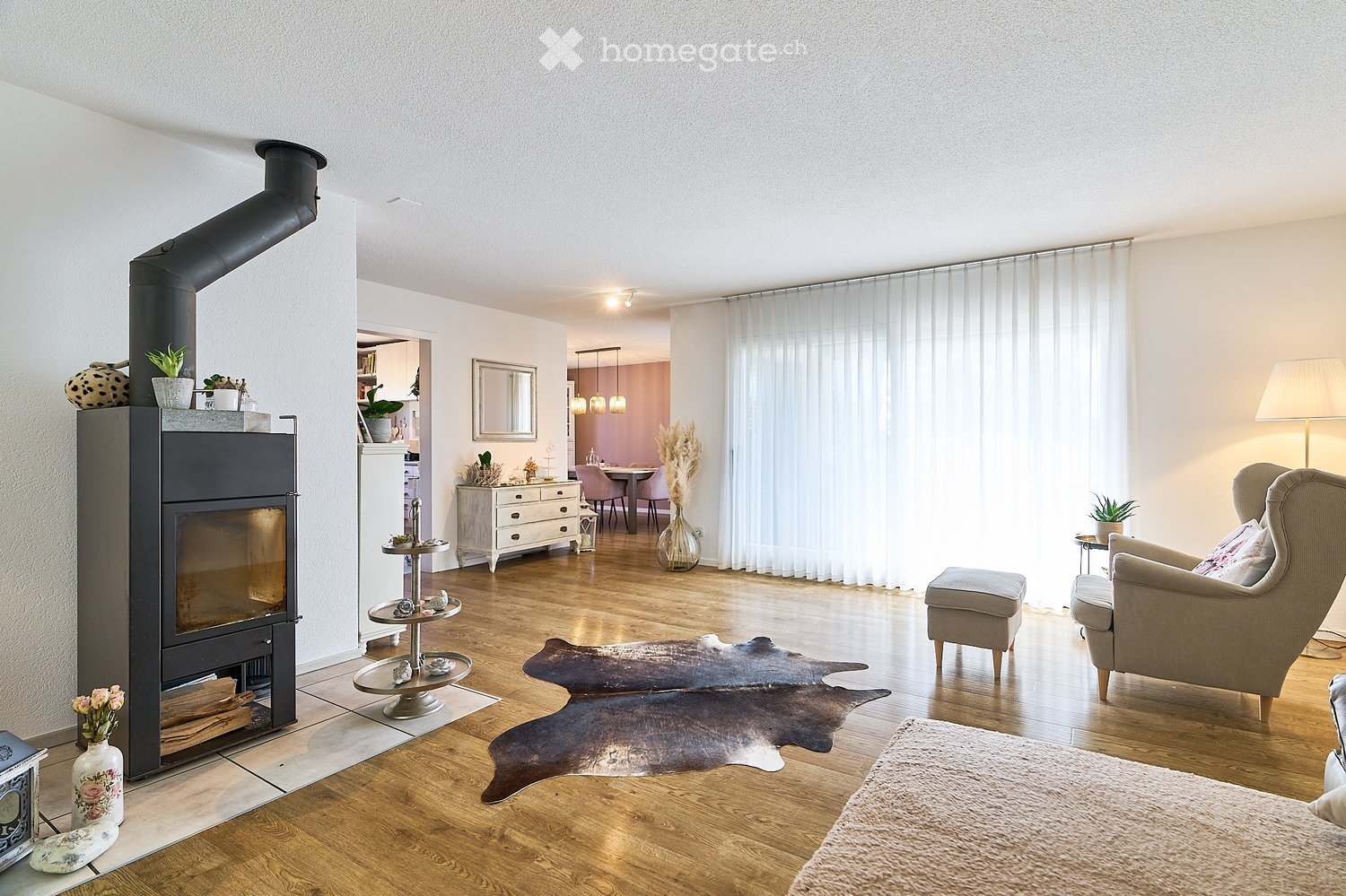 Modern living room with a fireplace, large windows, a sofa, armchair, ottoman, coffee table, and decorative vases.