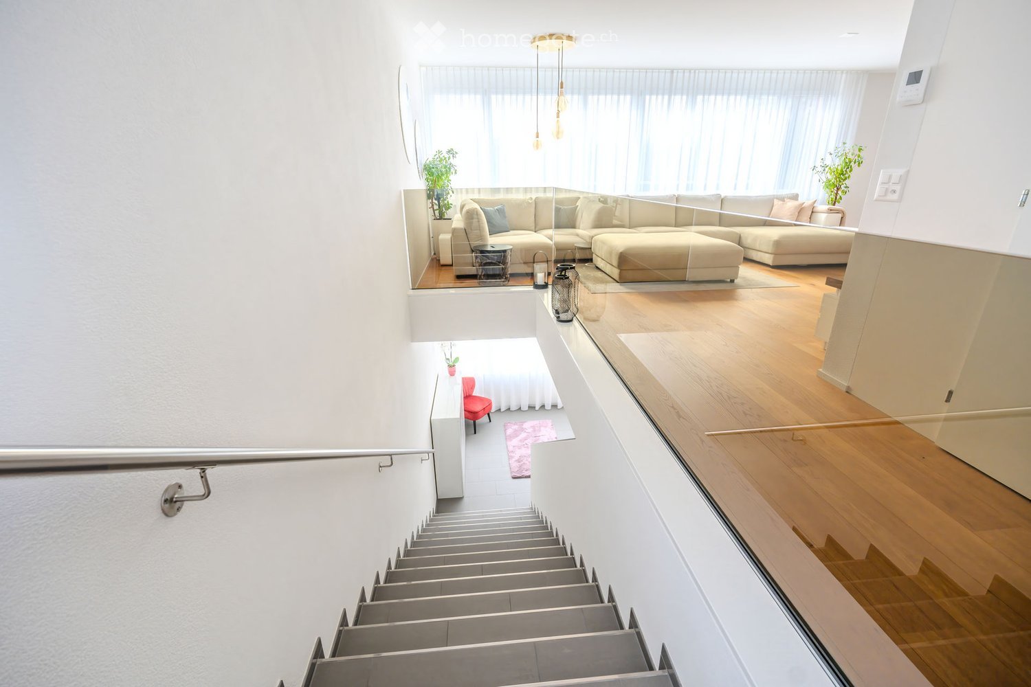 Stylishly designed staircase with handrail, glass flooring leading to a glass balcony with a lounge area featuring a couch and ottoman