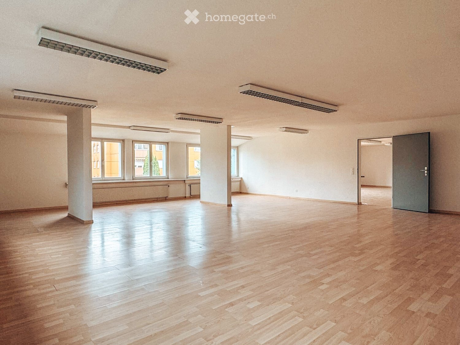 Empty room with wooden flooring, large windows, and white walls. No furniture or equipment present.
