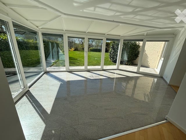 Empty conservatory with large glass windows and a polished concrete floor, allowing ample natural light.