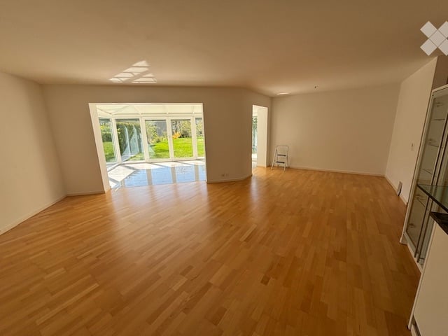 Empty room with wooden flooring, large glass door leading to a patio, and a small folding chair in the corner.